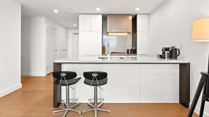 A modern kitchen with white cabinetry, a central island, two bar stools, and a coffee machine. - Chic 1-Bed with Pool by River, Ferry & Amenities (Wentworth Point)