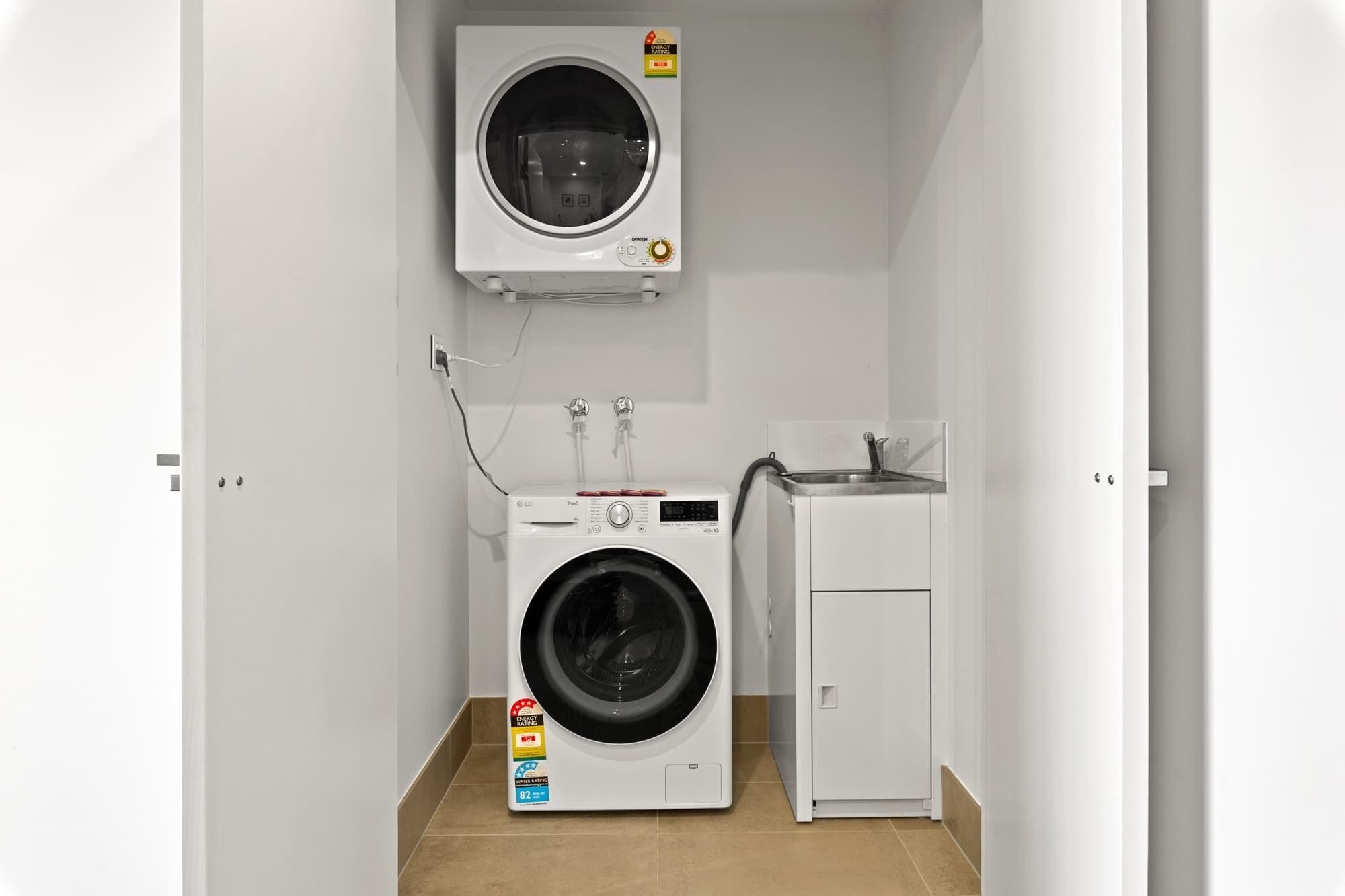A compact laundry room with a front-loading washing machine, a dryer, and a wall-mounted dryer.