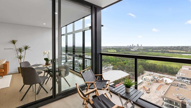 A modern balcony with a glass door, furnished with a table, chairs, and potted plants. - Chic 1-Bed with Pool by River, Ferry & Amenities (Wentworth Point)