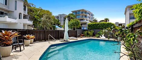 A swimming pool with a tiled deck, surrounded by potted plants and a wooden fence.