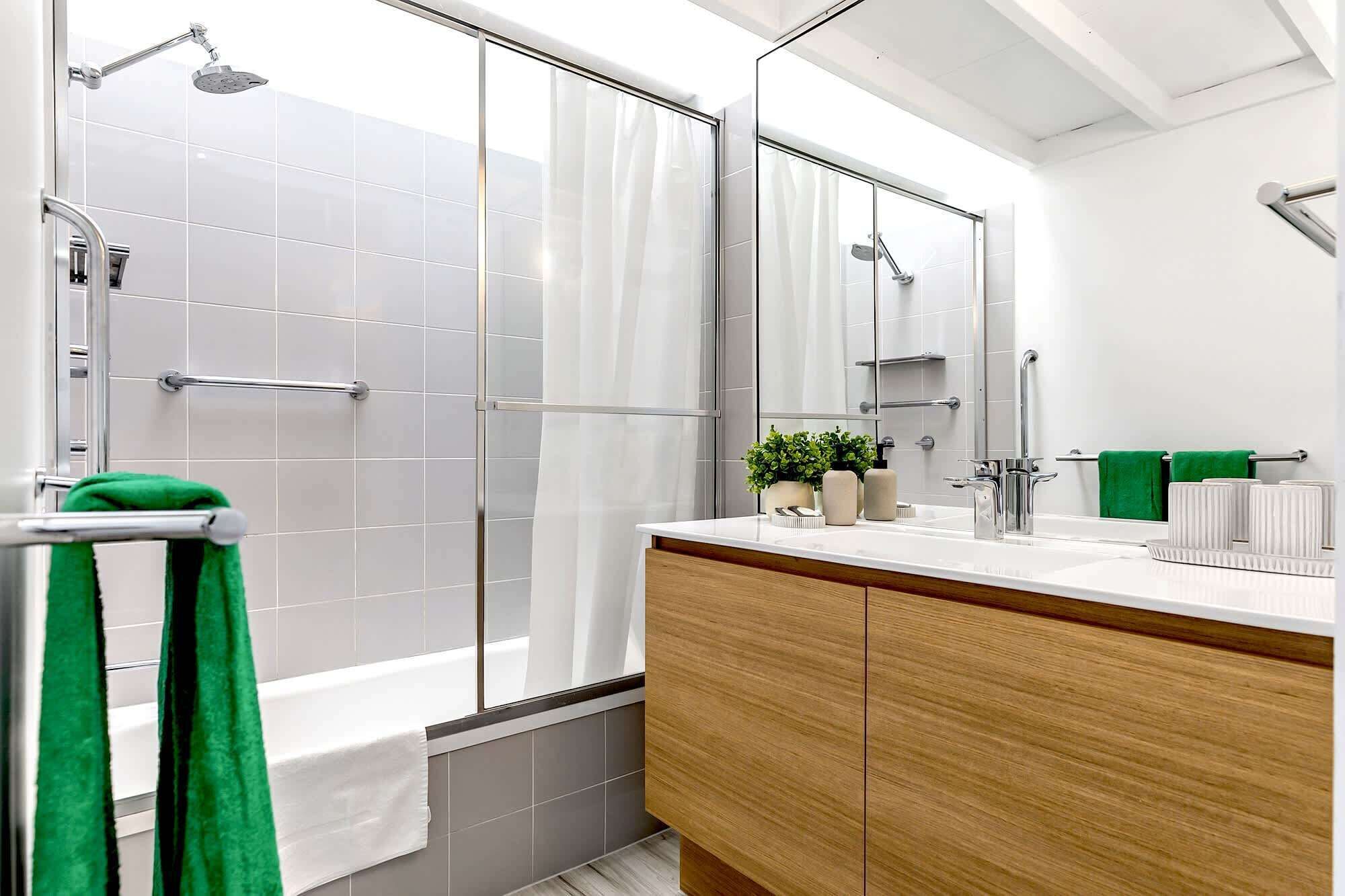 A modern bathroom with a glass shower enclosure, a wooden vanity, and a large mirror.