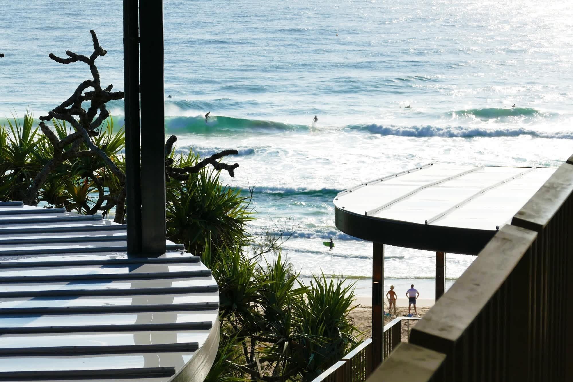 Blick auf einen Strand mit Sonnenschutzbereich und Palmen.
