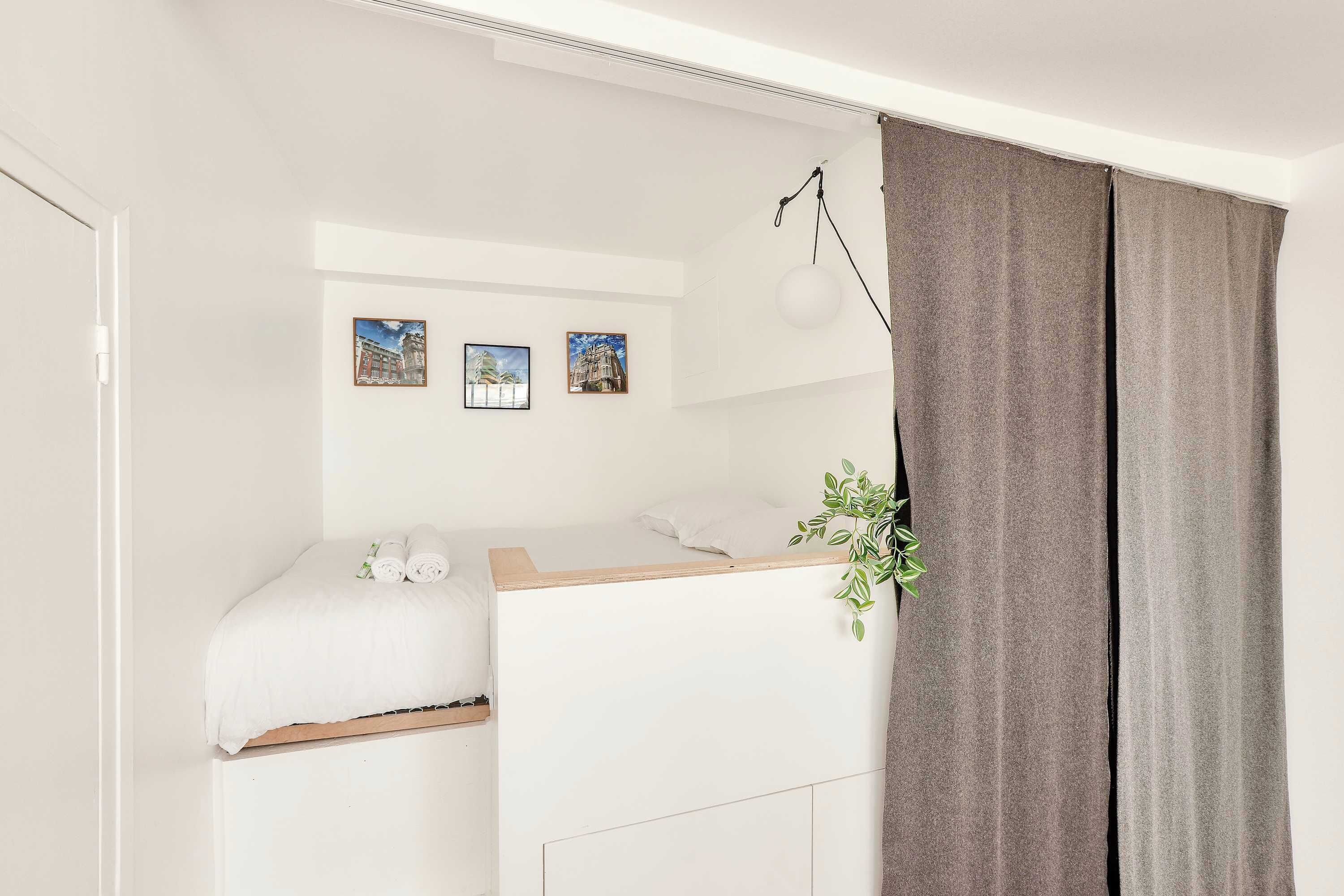 A bedroom with a bunk bed, a bedside table, a hanging plant, and three framed pictures on the wall.