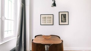 A dining area with a wooden table and chairs, a black pendant light, and two framed pictures on the wall.