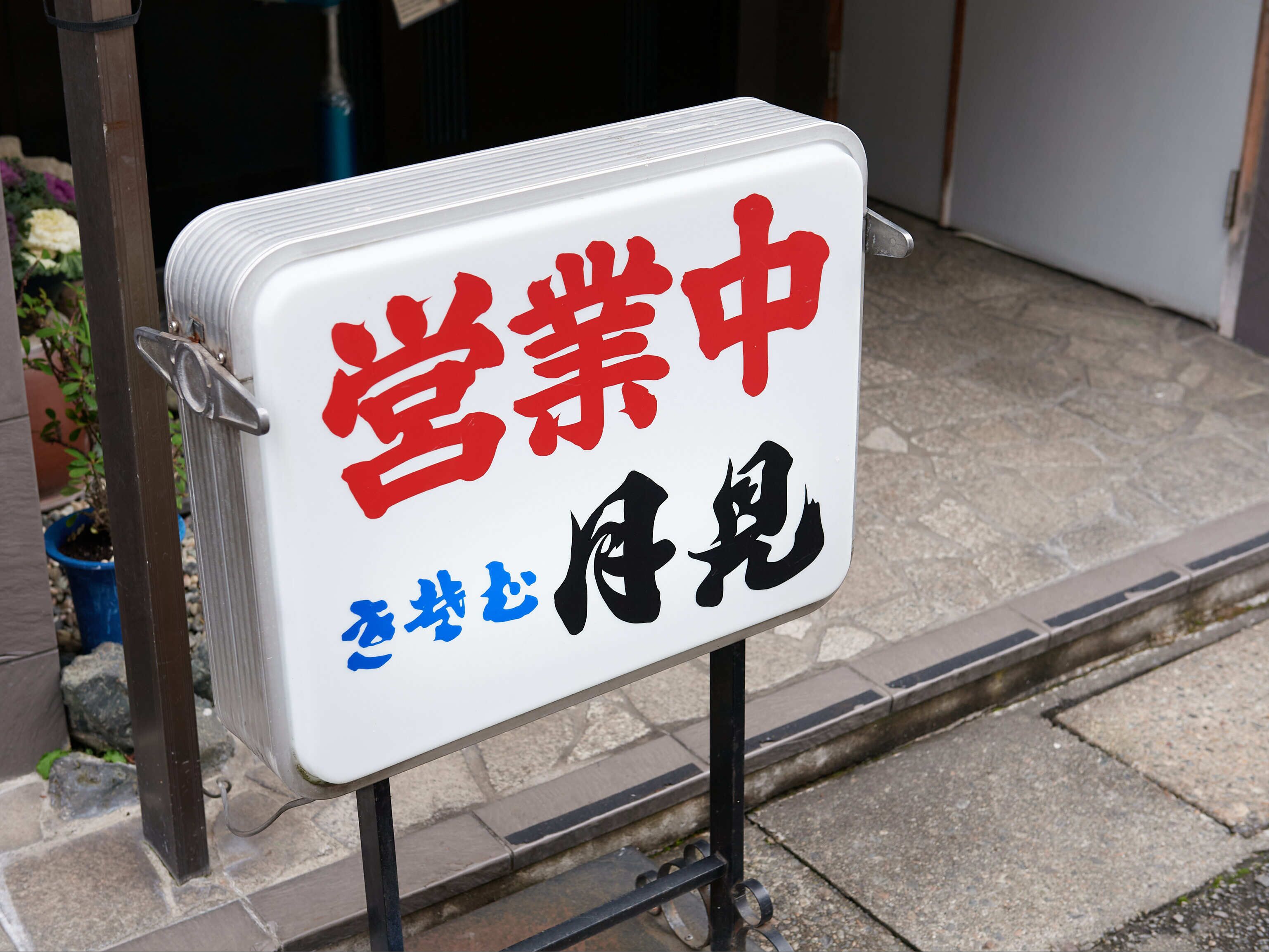 A sign with red and blue text on a white background, mounted on a metal stand.