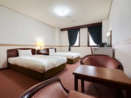 A hotel room with two beds, a desk, a chair, a desk lamp, a telephone, and a television.
