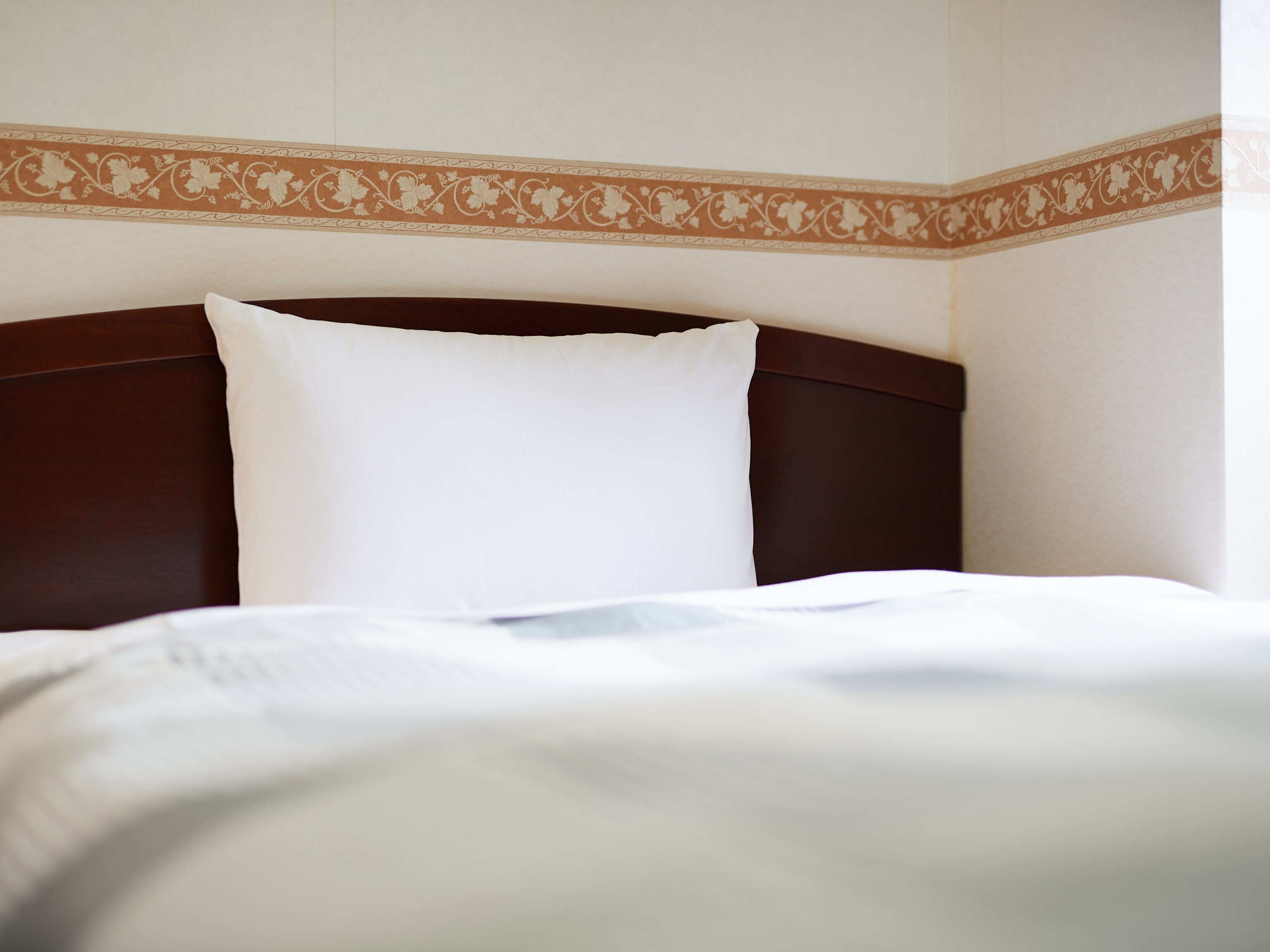 Un lit bien fait, avec un oreiller blanc et une tête de lit marron, dans une chambre d’hôtel.