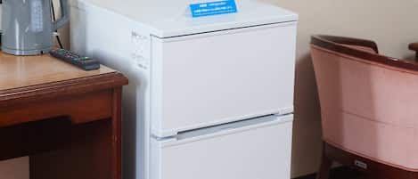 Ein weißer Kühlschrank mit blauer Beschriftung, eine Fernbedienung und ein Wasserkocher auf einem Holztisch.
