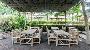 Un espace extérieur aménagé avec des meubles en bambou, abrité par un toit métallique et entouré de verdure.
