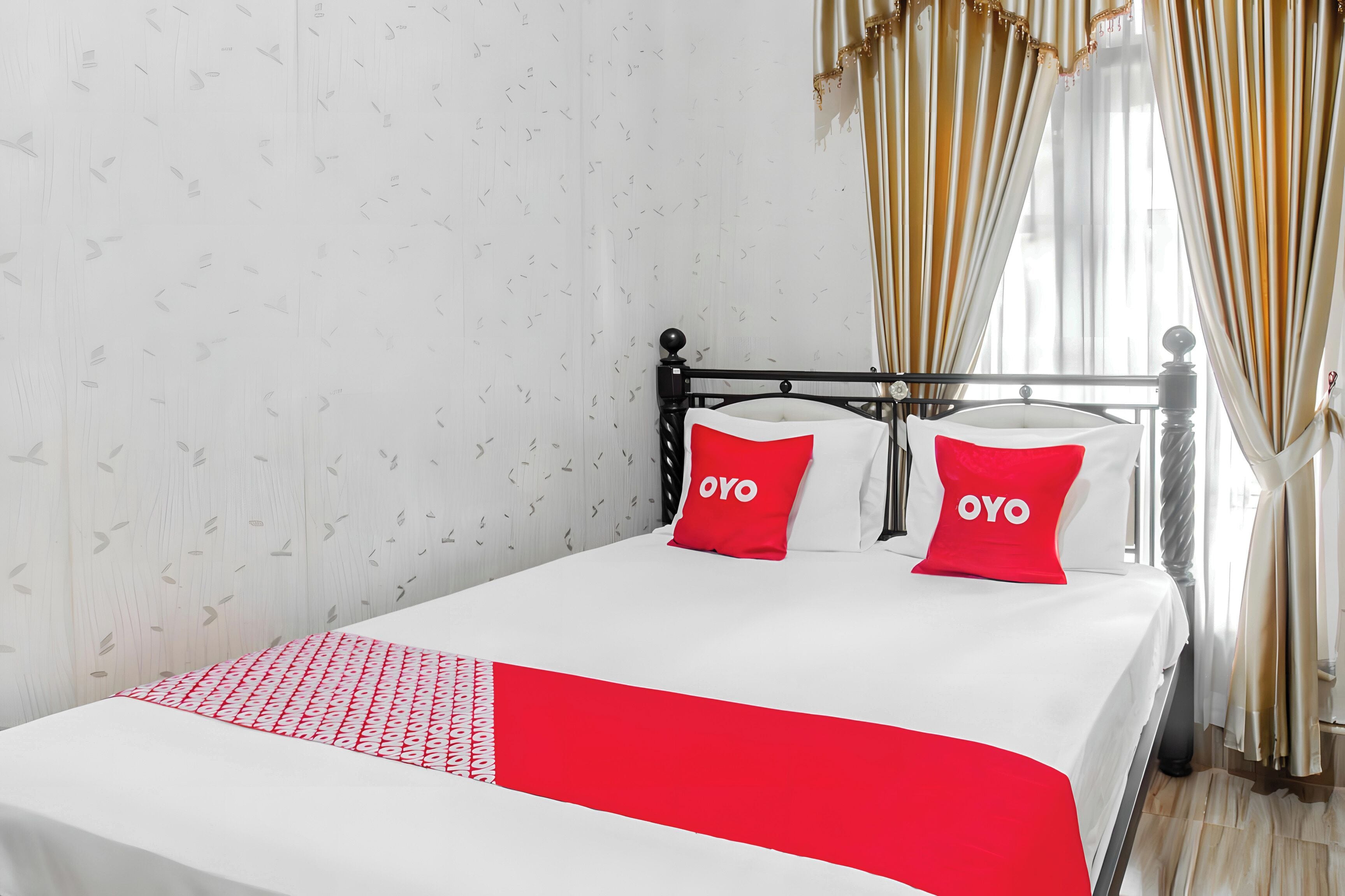 A bed with a white and red bedspread, two red pillows with the word 'OYO' on them, and a patterned wall.