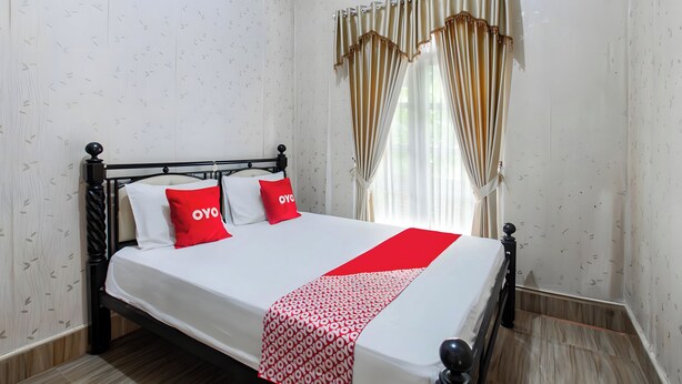 Un lit avec une couvre-lit blanche et rouge, deux oreillers et un coussin décoratif rouge avec l'inscription « OYO ».