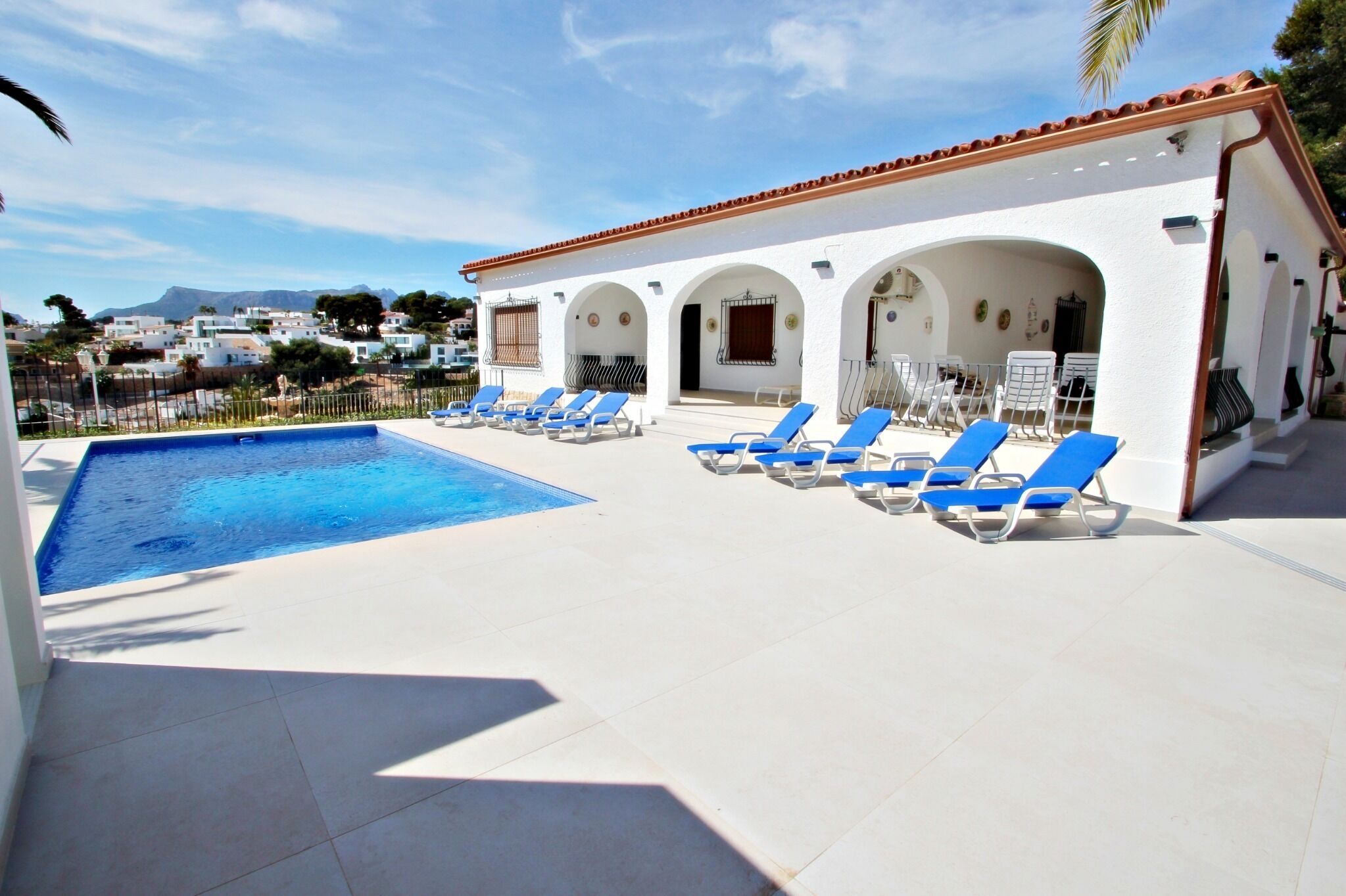 A swimming pool with blue lounge chairs and a white building with arches.