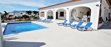 A swimming pool with blue lounge chairs and a white building with arches.