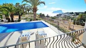 Une piscine dotée de chaises longues, de palmiers et offrant une vue sur la mer et les montagnes lointaines.