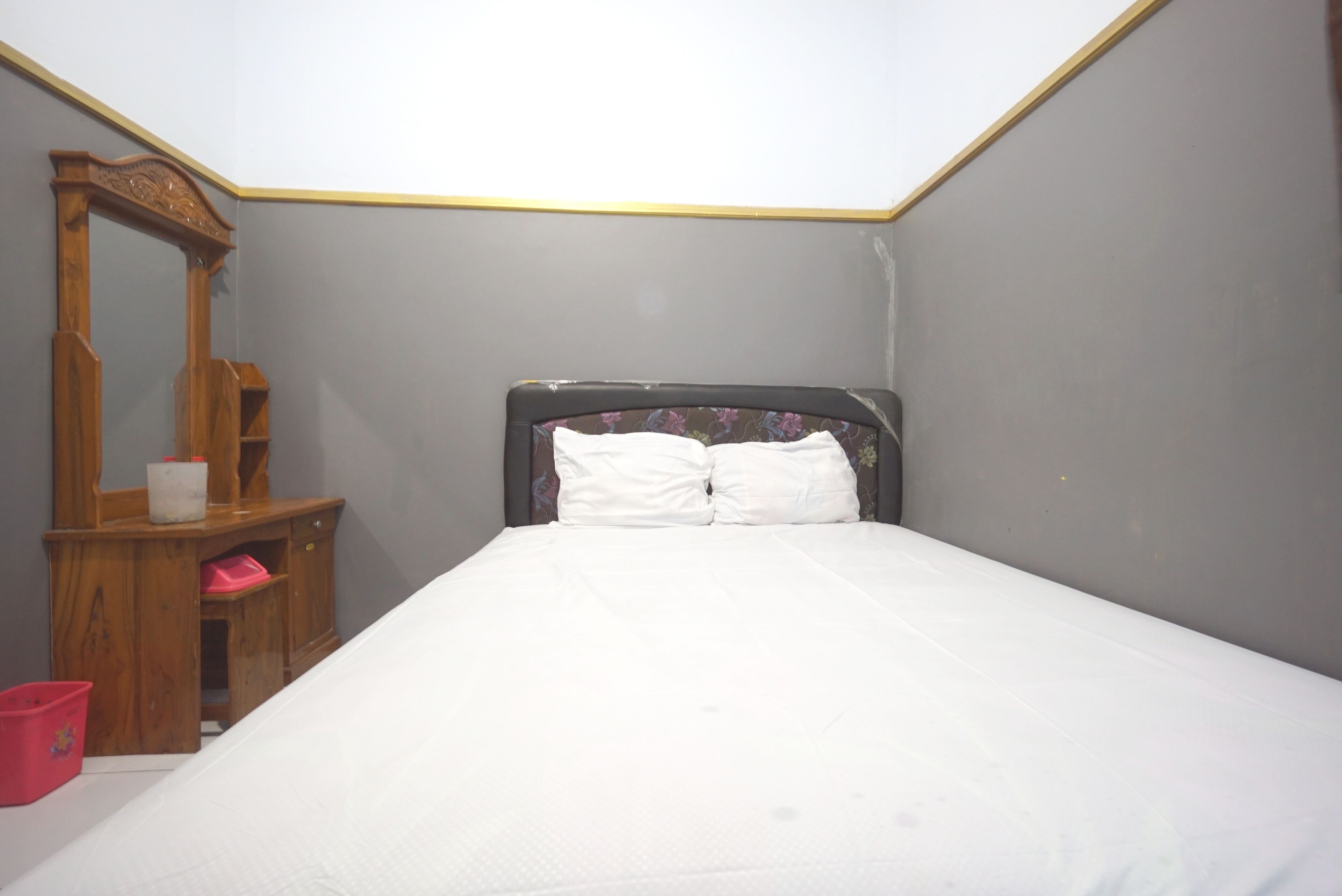 A bedroom with a bed, a wooden dresser, and a mirror.