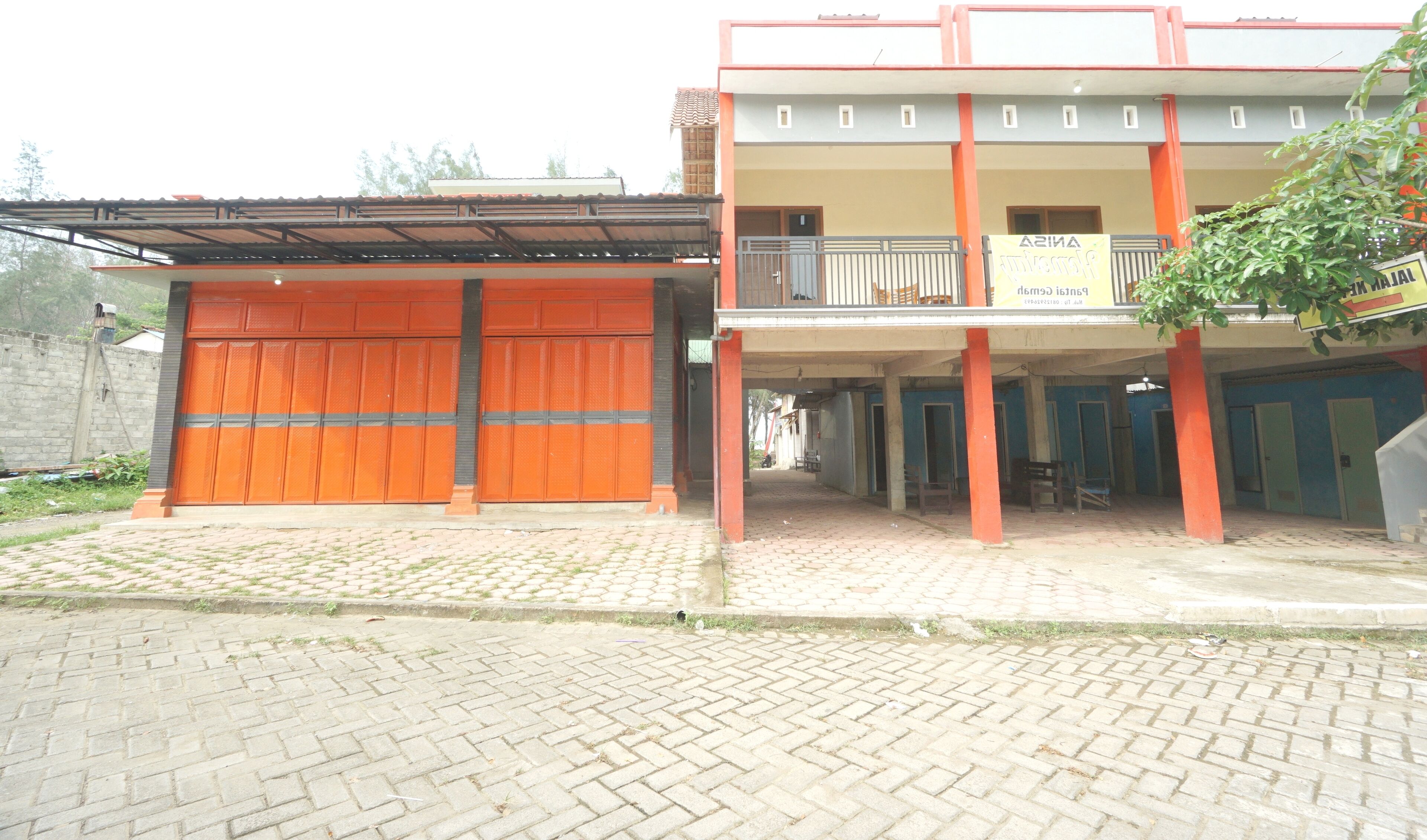 A building with a large orange garage door, a covered area with benches, and a signboard.