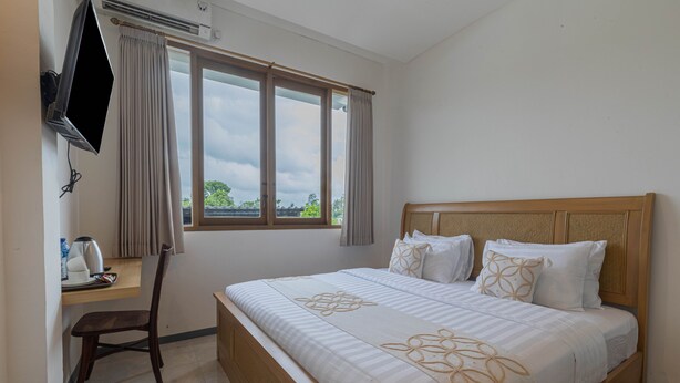 A hotel room with a bed, a desk, a chair, a TV, and a window with curtains. - ME Rooms Ubud (Ubud)
