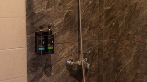 A bathroom with a marble wall, a showerhead, and two bottles of shampoo. - ME Rooms Ubud (Ubud)