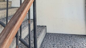 A staircase with a wooden handrail leading to a landing. On the landing, there are two signs: one indicating 'Rooms Upstairs' and another instructing to 'Ring the bell if you need help with your luggage.' - ME Rooms Ubud (Ubud)