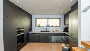 A modern kitchen with dark cabinetry, a large window, and a stainless steel refrigerator. - Seawhisper Villa in Paxi (Paxos)