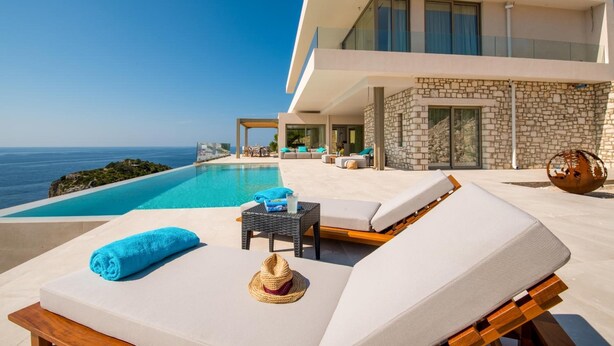 A modern villa with a pool overlooking the sea, featuring sun loungers, a small table, and a stone wall. - Seawhisper Villa in Paxi (Paxos)