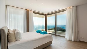 A modern hotel room with a large bed, a view of the ocean, and a balcony with curtains. - Seawhisper Villa in Paxi (Paxos)