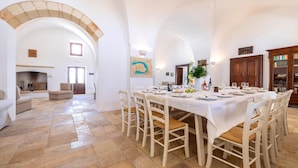 Un espace repas avec une longue table dressée pour six personnes, entourée de chaises blanches à assise tissée.