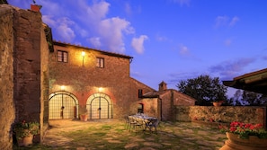 A stone building with two large arched windows and a table set for dining in the courtyard. - Villa Le Tornaie 14 Emma Villas (Monte San Savino)