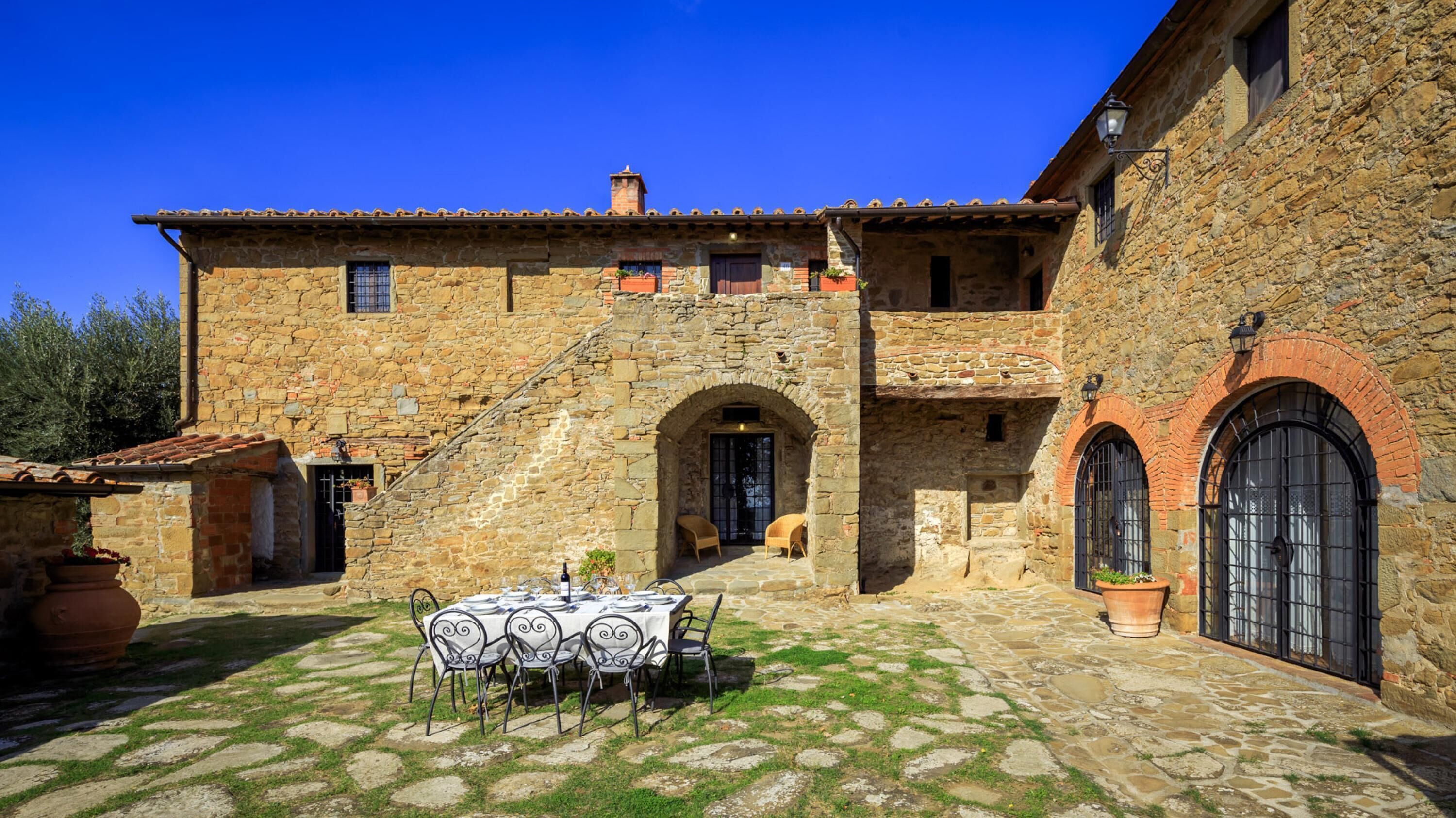 Un edificio de piedra con patio, mesas al aire libre y una escalera que lleva a la entrada.