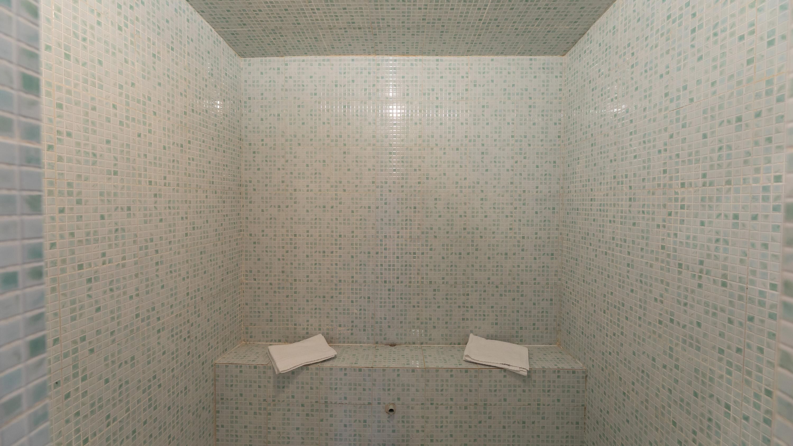 Une petite cabine de douche carrelée, avec un banc et deux serviettes.