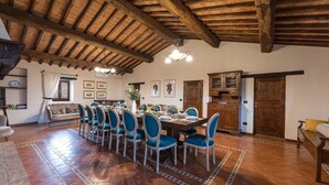 A dining area with a long wooden table set for six, surrounded by blue upholstered chairs. - Villa Le Tornaie 14 Emma Villas (Monte San Savino)