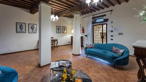A spacious living room with a blue sofa, a coffee table with drinks, and a dining area in the background. - Villa Le Tornaie 14 Emma Villas (Monte San Savino)
