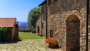 A stone building with arched doorways and a cobblestone pathway leading to a grassy area.