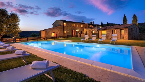 A stone building with a swimming pool, lounge chairs, and a well-maintained lawn.
