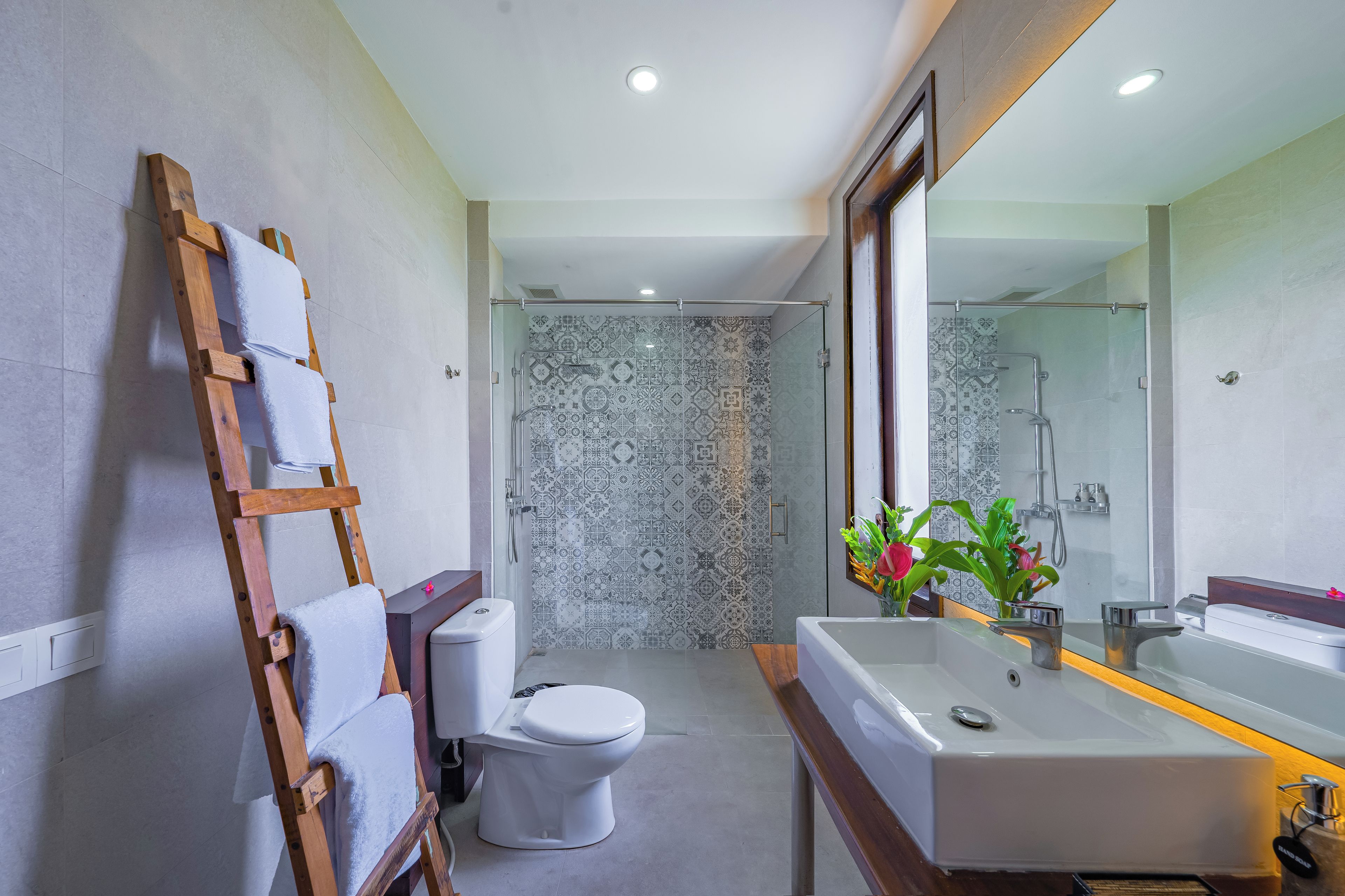Een moderne badkamer met een houten ladder, een wit toilet en een groot wastafelmeubel met een spiegel erboven.