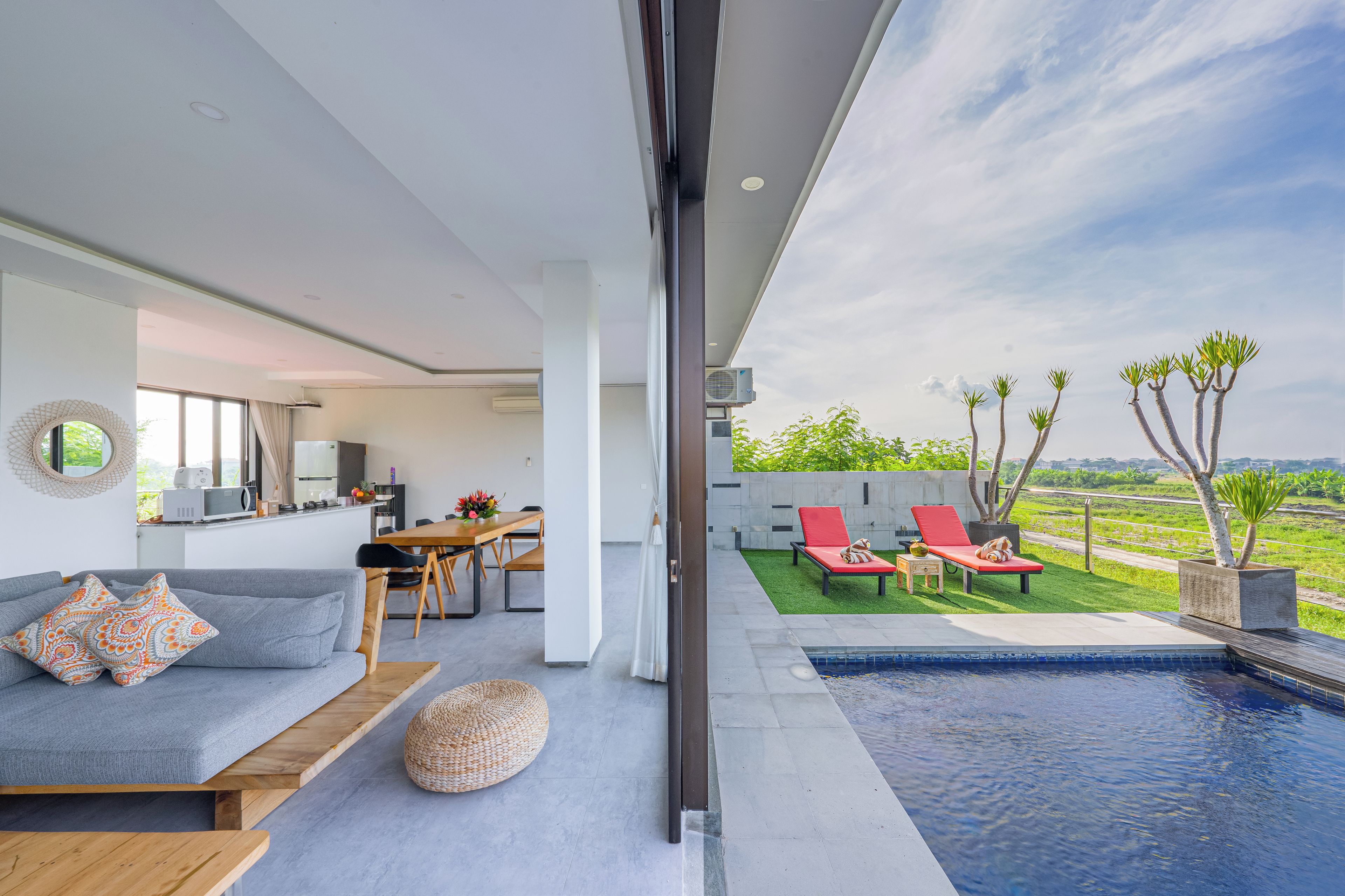 A modern living room with a sofa, dining table, and a view of a swimming pool and garden.