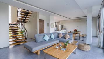 A modern living room with a grey sofa, wooden coffee table, and a spiral staircase.
