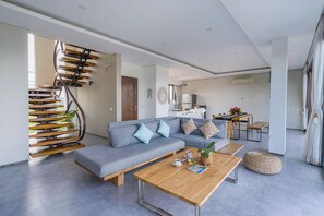 A modern living room with a grey sofa, wooden coffee table, and a spiral staircase. - Villa Emilia Seminyak by Nagisa Bali (Kerobokan)