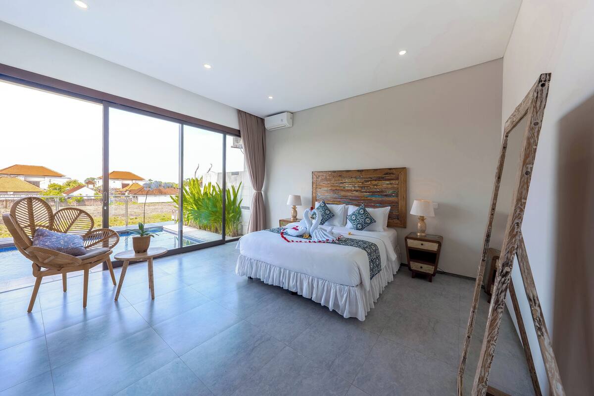 Ein modernes Hotelzimmer mit einem großen Bett, einem Balkon mit Blick und einem Holzsessel.