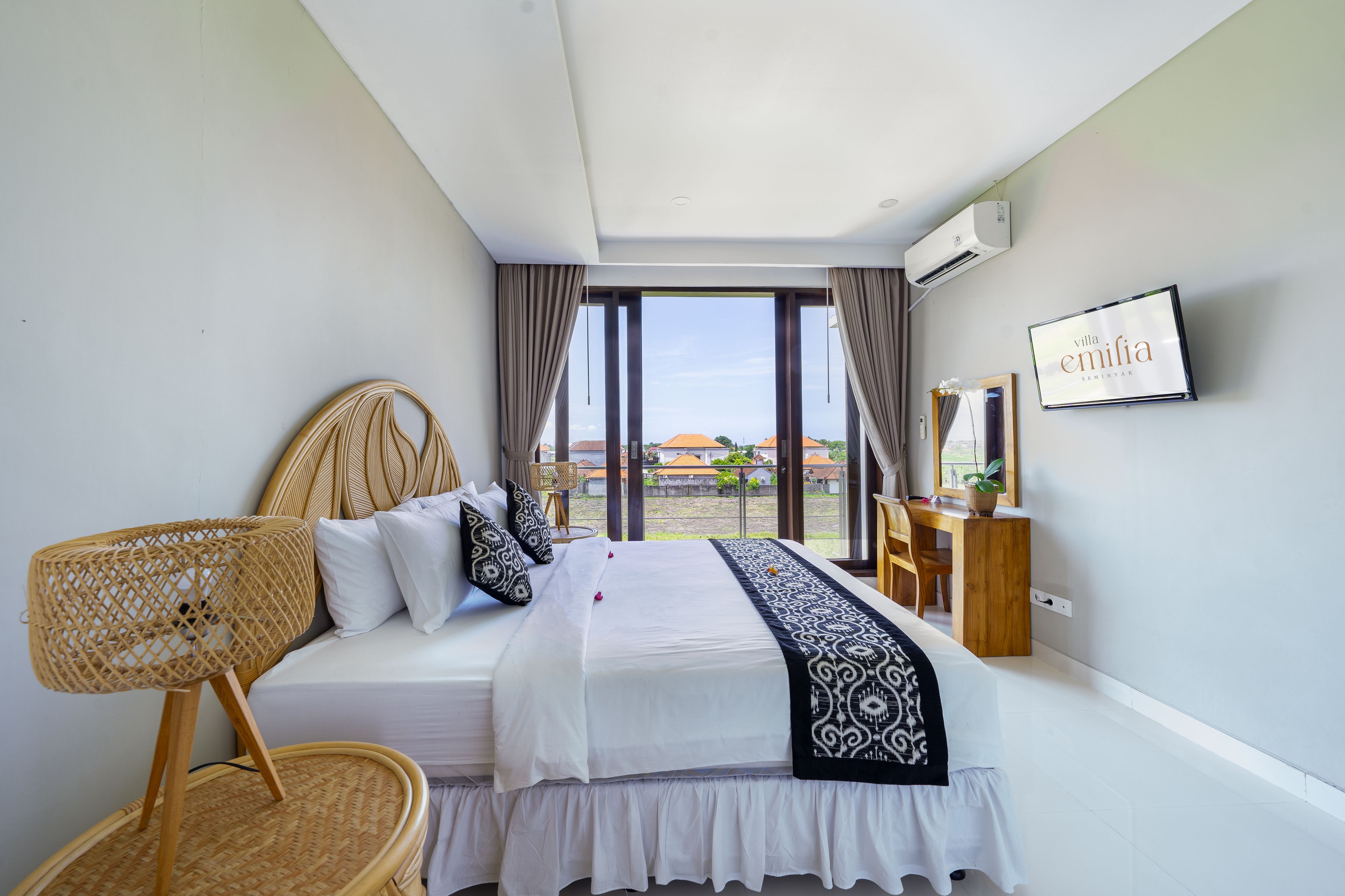 A bedroom with a bed, a desk, a chair, and a large window with a view.