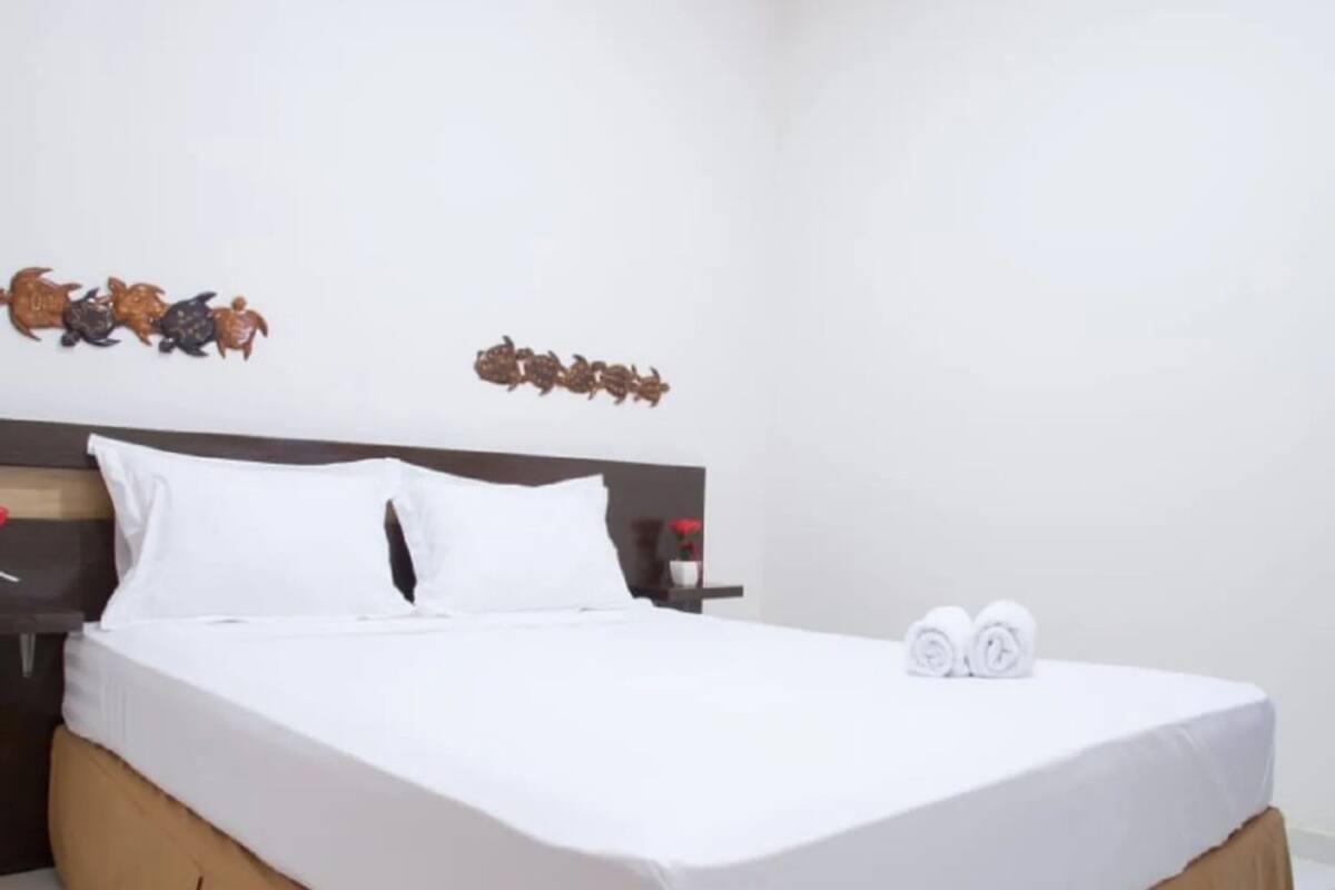 Un lit bien fait, avec du linge de lit blanc et une couvre-lit marron, une tête de lit en bois et des décorations murales représentant des poissons.