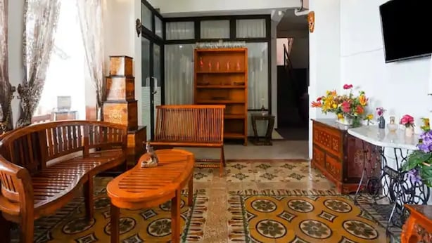 A living room with a sofa, a wooden coffee table, a bookshelf, and a TV mounted on the wall. - Hotel Djagalan Raya  (Surabaya)