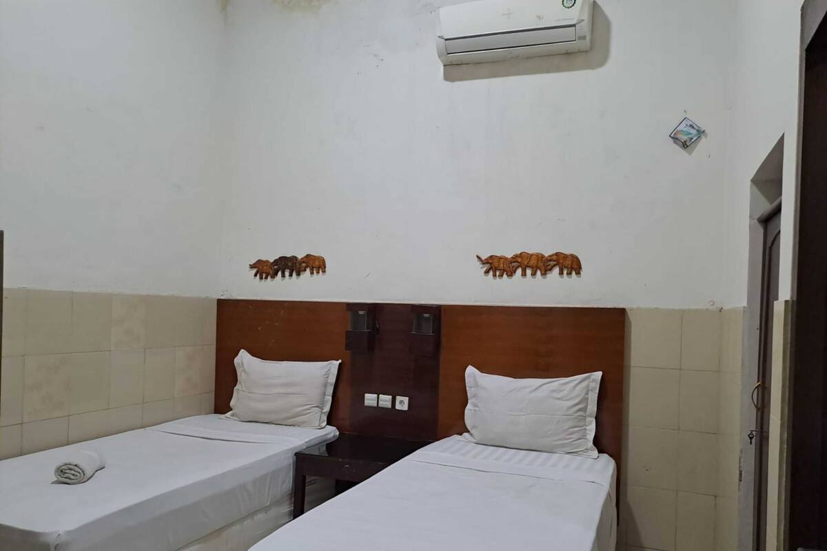Une chambre d’hôtel avec deux lits simples, une tête de lit en bois, un appareil de climatisation et des figurines d’animaux décoratives fixées au mur.