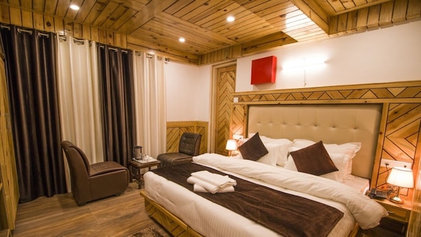 Ein Hotelzimmer mit zwei Betten, einem Sessel, einem Nachttisch und einer Holzbalkendecke.