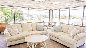 A spacious room with two beige sofas, a small round table, and large windows offering a view of the outside.