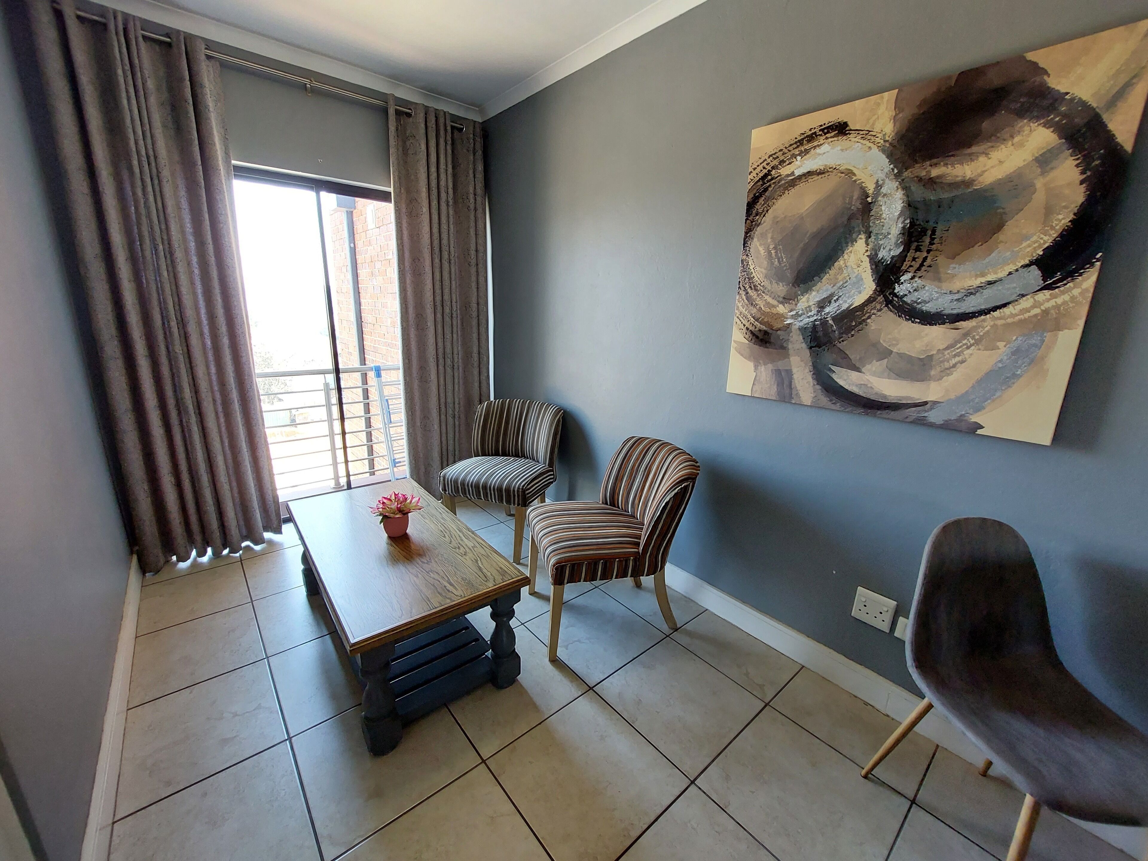 Una habitación con una mesa de comedor, dos sillas a rayas, una planta en maceta y un cuadro abstracto grande en la pared.