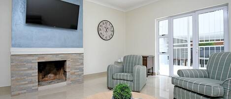 A living room with a fireplace, a flat-screen TV, a clock, striped armchairs, and a round coffee table with a plant.