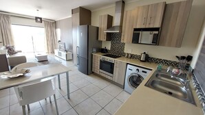 A modern kitchen with a dining area, a washing machine, and a microwave. - Zwelakho Luxury  furnished apartments (Sandton)