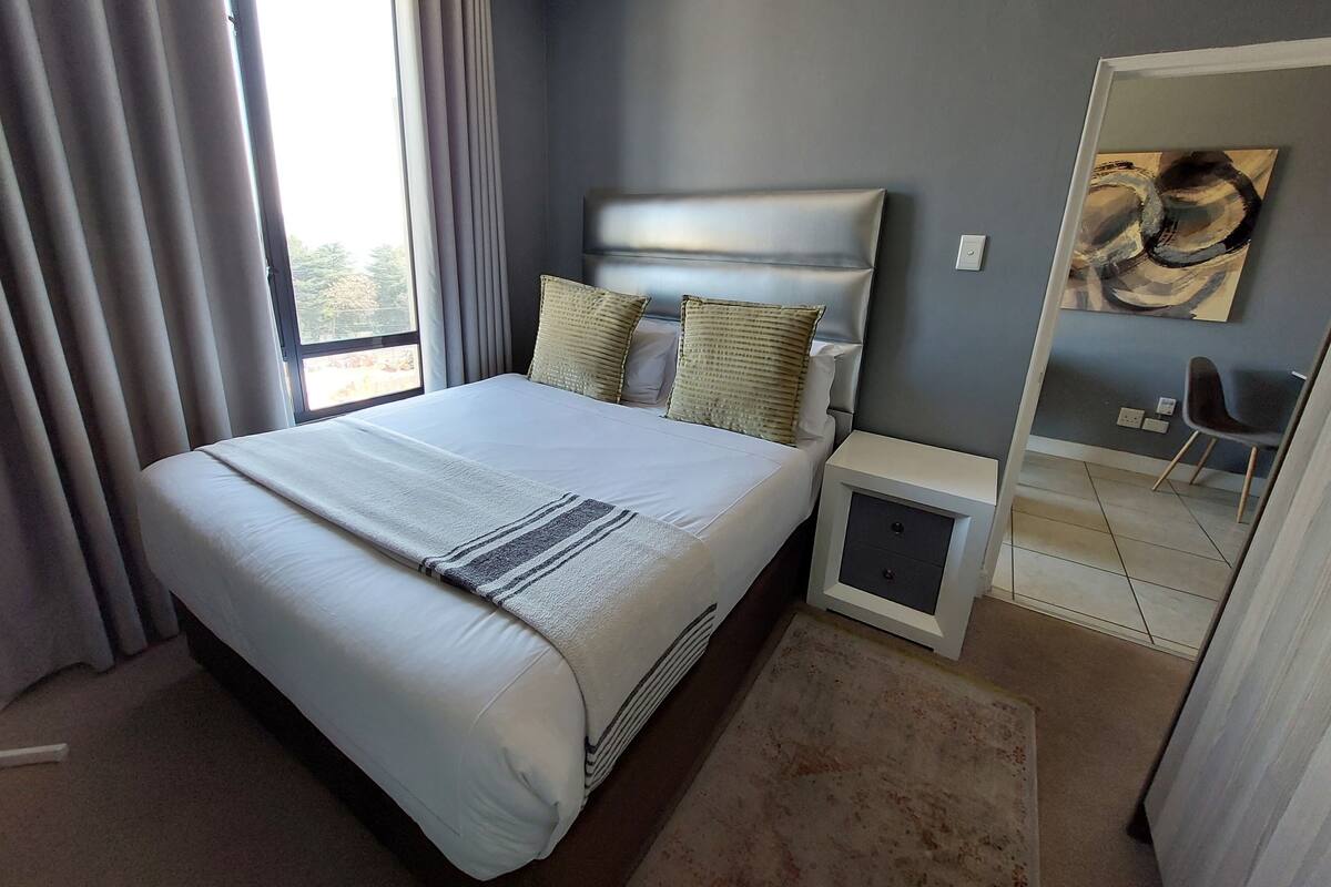 Ein modernes Hotelzimmer mit einem großen Bett, einem Nachttisch, einem kleinen Schreibtisch und einem Stuhl.