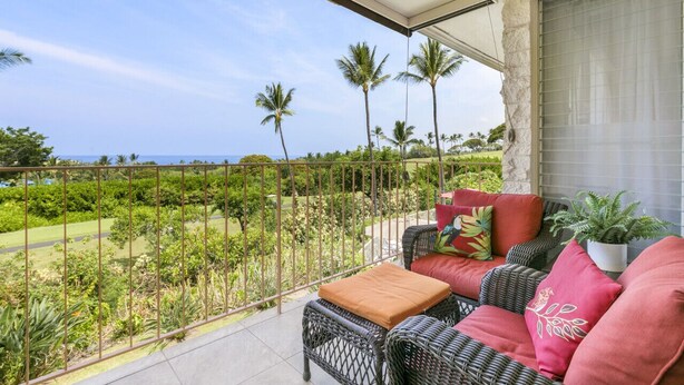 A balcony with wicker furniture, a view of the ocean, and tropical vegetation. - Ocean View Kona Condo | Relax, Unwind & Enjoy Island Life (Kailua-Kona)
